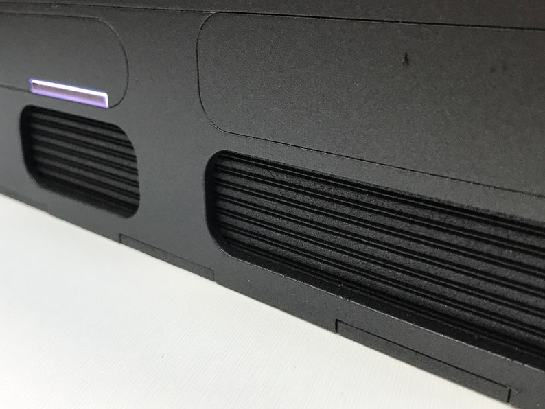 May include: Close-up of a black rectangular object with two rectangular vents and a thin, light blue strip. The vents have a ribbed design.