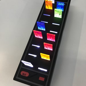 May include: A black electronic device with a red button and a white light. The device has a series of transparent colored panels with text on them, including "01-400".