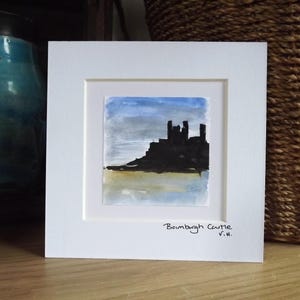 May include: A framed watercolour painting of Bamburgh Castle. The artwork shows the castle's silhouette against a blue and grey sky, with a yellow and blue foreground. The painting is signed "V.H." and is set in a white mount.
