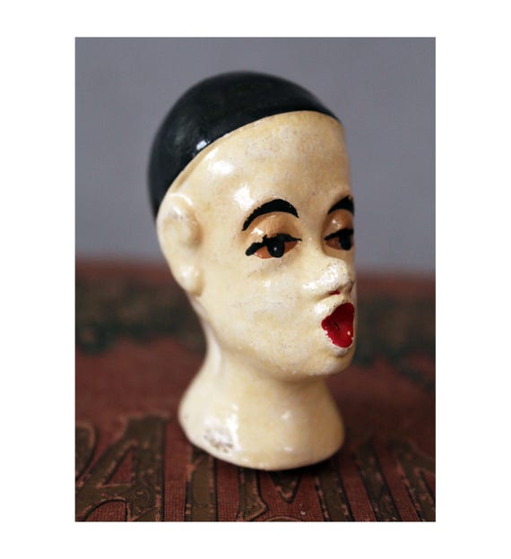 A hand-painted vintage French Pierrot doll head — eerie, theatrical, and deeply specific in the best way; a true collector's curiosity.