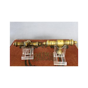 以下が含まれることがあります： 大砲の形をしたアンティーク真鍮製のドアノブ2個。ノブは透明なプラスチックスタンドに飾られています。