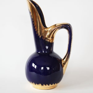 May include: A cobalt blue ceramic pitcher with a gold-trimmed spout and handle. The pitcher has a rounded body and a delicate, curved spout.