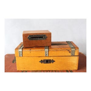 Peut inclure: Deux boîtes en bois avec des accents métalliques. La boîte du haut a une fente pour les pièces de monnaie et la boîte du bas a un trou de serrure. Les deux boîtes sont en bois clair.