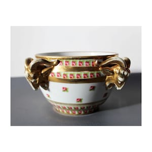 Könnte beinhalten: Eine weiße Porzellanschale mit goldenen Verzierungen und einem Muster aus rosa Rosen. Die Schale hat zwei goldene Tierkopfgriffe.