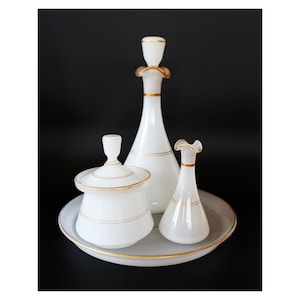 Könnte beinhalten: Ein weißes Glas-Schminkset mit goldenen Verzierungen. Das Set enthält eine Flasche, ein Glas, eine kleine Vase und ein Tablett.