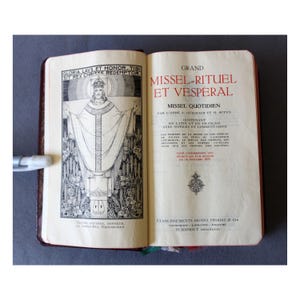 May include: An open book with a brown leather cover. The left page features a black and white illustration of a religious figure. The right page has text in French, including the title "Grand Missel-Rituel et Vespéral."