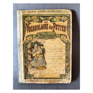 Op de afbeelding: Oud Frans kinderwoordenboek, "Le Vocabulaire des Petits" door M. Fournier. De omslag toont illustraties van kinderen en bloemmotieven, met Franse tekst. Het boek vertoont tekenen van slijtage en heeft een vintage uitstraling.