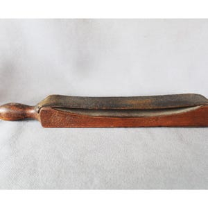 以下が含まれることがあります： 木製のハンドルと革の表面を備えた、ヴィンテージのストレートカミソリ用ストロップ。ストロップは長方形で、端が湾曲しており、カミソリを研ぐように設計されています。ハンドルは丸みを帯びた形状で、木製のベースに取り付けられています。