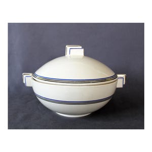 Può includere: Un piatto da portata in ceramica bianca con coperchio. Il piatto ha un motivo geometrico blu e oro attorno al bordo.