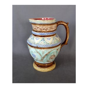 May include: A brown and blue ceramic pitcher with a floral design. The pitcher has a wide base and a handle.