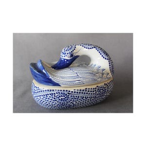 Könnte beinhalten: Eine blaue und weiße Keramik-Schmuckschatulle in Schwanenform mit Deckel. Der Schwan hat ein detailliertes Design aus blauen und weißen Punkten und Spiralen.
