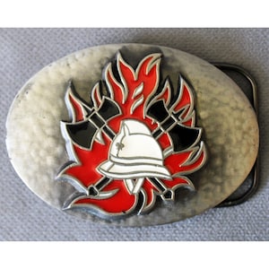 Peut inclure: Une boucle de ceinture ovale avec une finition argentée martelée. Le centre présente un emblème en relief représentant un casque de pompier blanc placé devant deux haches noires croisées, le tout sur un motif de flammes rouge vif.