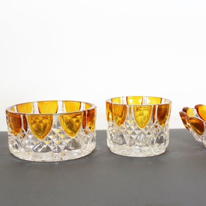 Op de afbeelding: Vier glazen kommen met amberkleurige randen. De kommen zijn van verschillende groottes en vormen, waarbij de grootste een cilinder is en de kleinste een ondiepe schaal.