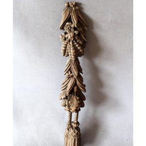 Peut inclure: Élément décoratif en bois sculpté avec un design vertical. La pièce présente des sculptures détaillées de feuilles, de fleurs et une base en forme de gland. Le bois est de couleur marron clair naturel.