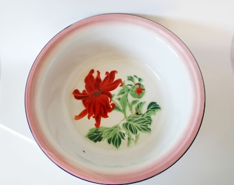 May include: A white enamel bowl with a pink and blue rim. The bowl features a red flower with green leaves and a small red fruit.