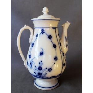 Op de afbeelding: Witte porseleinen koffiepot met een deksel, handvat en tuit. De pot is versierd met blauwe bloempatronen en lijnen. De basis en de rand zijn ook blauw geaccentueerd. Een klassiek ontwerp voor het serveren van koffie of thee.