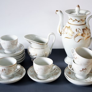 Può includere: Un set da tè in porcellana bianca con disegni floreali dorati. Il set comprende una teiera, un creamer e sei tazze e piattini.