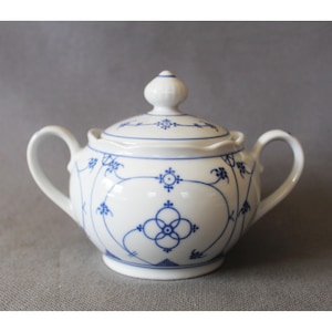May include: White porcelain sugar bowl with a lid, featuring blue floral and geometric patterns. The bowl has two handles and a knob on the lid. The design is symmetrical and delicate, suitable for serving sugar or other condiments.