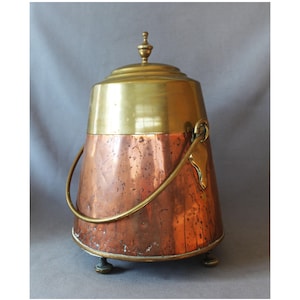 Può includere: Un contenitore vintage in rame e ottone con coperchio e manico. Il contenitore ha un corpo in rame e un coperchio e manico in ottone. Poggia su tre piccoli piedini in ottone. Il manico è fissato con un elemento decorativo a forma di foglia.