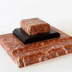 Könnte beinhalten: Ein dreistufiges Tintenfass aus Marmor und Schwarz. Die oberste Stufe ist ein rechteckiges Stück roten Marmors mit weißen Adern. Die mittlere Stufe ist ein schwarzes rechteckiges Tablett. Die unterste Stufe ist ein größeres rechteckiges Stück roten Marmors mit weißen Adern.