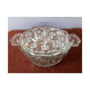 May include: A clear glass flower frog. The round bowl has a lid with multiple holes. The bowl has a scalloped edge and decorative handles. The flower frog is designed to hold flowers in place.