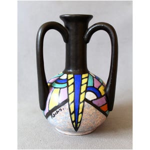 May include: A ceramic vase with two tall black handles and a narrow neck. The bulbous body features a colorful geometric pattern of blue, yellow, pink, and turquoise segments outlined in black, with the signature P. Dubois visible on the side.