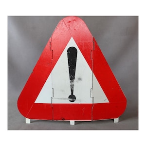 May include: A triangular warning sign featuring a bold red border and a white center with a black exclamation mark symbol. The sign is constructed from three vertical panels joined together, with small white support feet at the bottom edge.