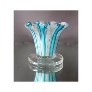 Pode incluir: Um vaso de vidro transparente com a parte superior alargada e uma base circular. O vaso apresenta riscas verticais turquesa e brancas. A borda do vaso tem uma borda franzida. O vaso é refletido na superfície abaixo.