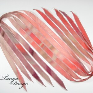 May include: A collection of ten thin, pink, and beige silk ribbons with a white edge. The ribbons are arranged in a fan shape and have a subtle tie-dye pattern.