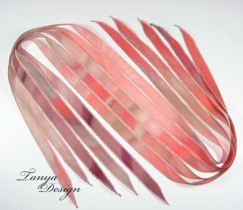 May include: A collection of ten thin, pink, and beige silk ribbons with a white edge. The ribbons are arranged in a fan shape and have a subtle tie-dye pattern.