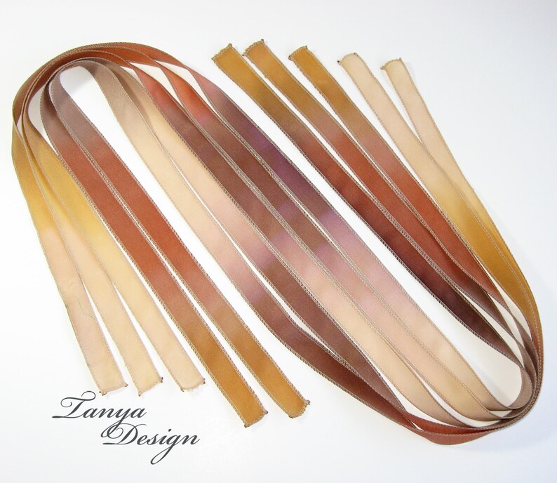 May include: Assortment of ten thin, hand-dyed silk ribbons in shades of brown, beige, and cream. The ribbons are arranged in a fan shape and have a subtle ombre effect.