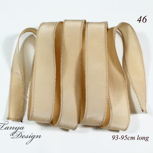 May include: A beige satin ribbon, 93-95cm long. The ribbon is folded in a pile and has a subtle sheen.