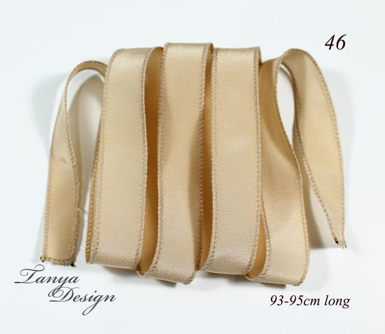 May include: A beige satin ribbon, 93-95cm long. The ribbon is folded in a pile and has a subtle sheen.