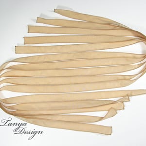 May include: A bundle of 12 beige satin ribbon strips, each with a stitched edge. The ribbons are arranged in a fan shape, with the ends of the ribbons overlapping.