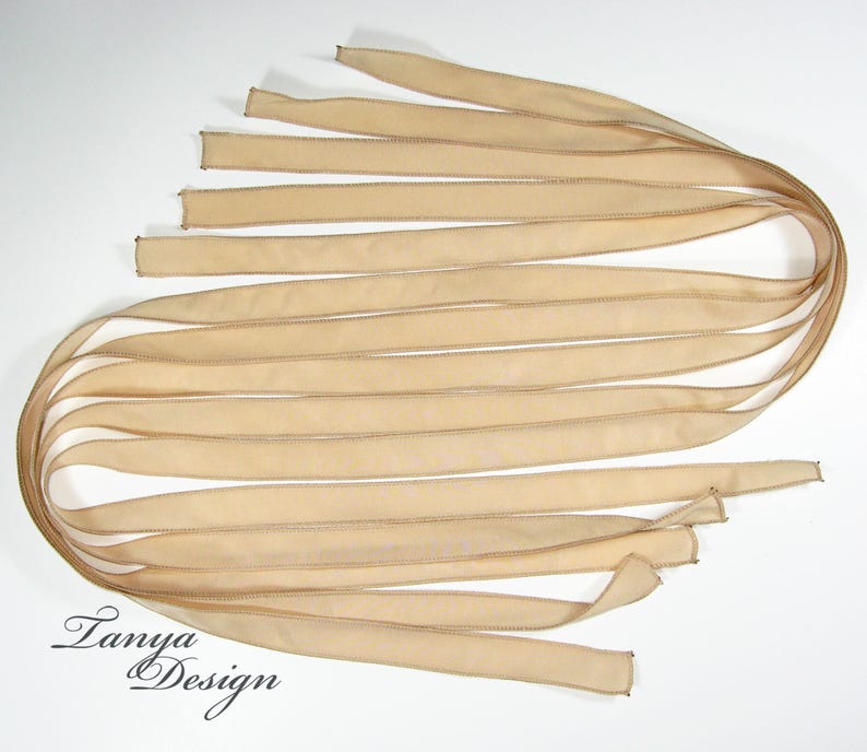 May include: A bundle of 12 beige satin ribbon strips, each with a stitched edge. The ribbons are arranged in a fan shape, with the ends of the ribbons overlapping.