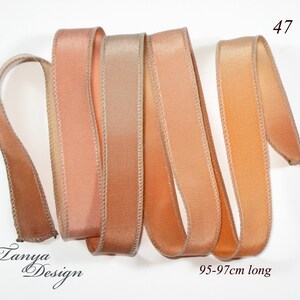 May include: Four strands of peach and beige ombre satin ribbon, each approximately 95-97 cm long. The ribbon has a subtle sheen and a delicate, stitched edge.