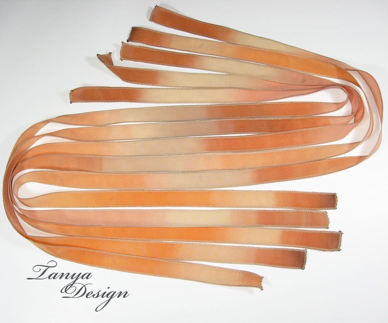 May include: A bundle of ten ombre ribbon strips in shades of peach, orange, and cream. The ribbon is a soft, sheer fabric with a subtle sheen.