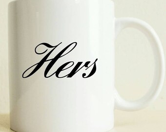 May include: White ceramic mug with a black cursive inscription that reads "Hers".