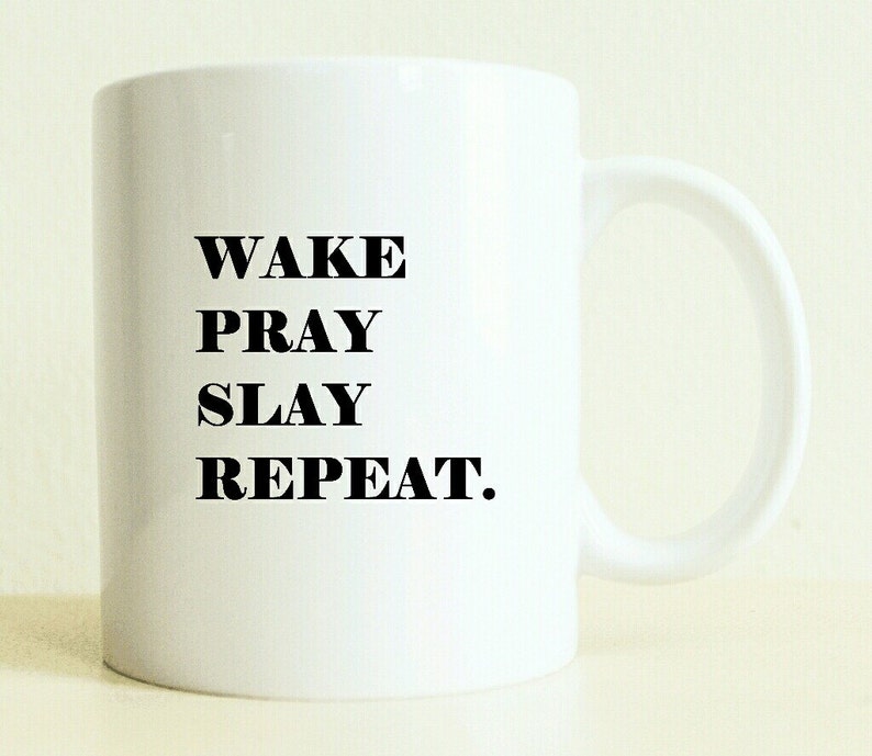 K&ouml;nnte beinhalten: Wei&szlig;e Keramik-Kaffeetasse mit schwarzem Text, der "WAKE PRAY SLAY REPEAT." lautet.