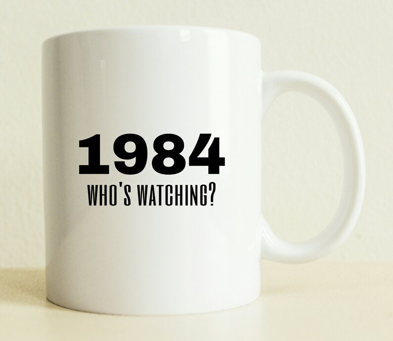 May include: White ceramic coffee mug with black text that reads "1984 Who's Watching?"