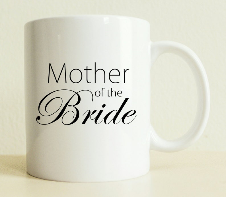 May include: White ceramic mug with black text that reads "Mother of the Bride".