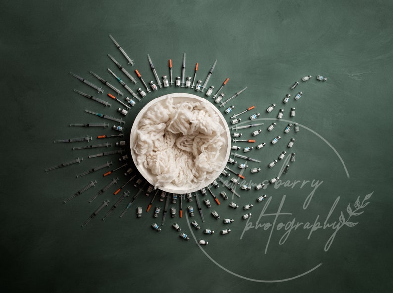 May include: A white bowl filled with white yarn, surrounded by a circle of syringes and vials on a green background. The text "emrys barry photography" is written in white on the bottom right of the image.
