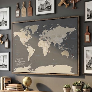 May include: A living room with a gray sofa, wooden shelf, and a wall decorated with framed black and white photos of landmarks, wooden airplane models, and a large world map. The map is framed and has push pins marking locations.