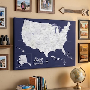 May include: A navy blue map of the United States with white detailing and the text "The Adventures of the Ingarten Family" is displayed on a wall. Several framed photos, a wooden arrow, and a globe are also on display.