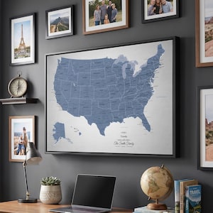 May include: A home office with a wooden desk, a laptop, and a globe. A large framed map of the United States hangs on the wall, surrounded by framed family photos and a picture of the Eiffel Tower. A small clock sits on a shelf.