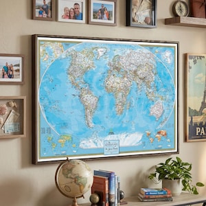 May include: A large framed world map with a blue ocean and detailed landmasses hangs on a beige wall. Several framed photos, a shelf with a compass and journals, and a Paris poster are also displayed. A globe and books sit on a table.