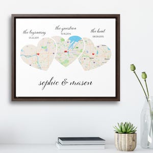 May include: A framed print featuring three heart-shaped map sections, each representing a significant life event. The text includes dates and phrases like "the beginning," "the question," and "the knot," along with the names "sophie & mason."