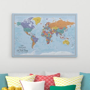 May include: A light blue world map with colorful countries and a white border. The map is hanging on a white wall above a white couch with colorful pillows. The text "The Smith Family World Travels" is printed at the bottom of the map.