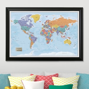 May include: A framed world map with a light blue background and colorful country borders. The map is in a black frame and has a small white label in the bottom left corner that reads "The Adventures of Mike & Brenda".