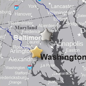May include: A gray map of the Mid-Atlantic region with the cities of Baltimore and Washington, D.C. highlighted. A gold star and a silver star mark locations on the map. The map includes the text "Maryland" and "Washington".